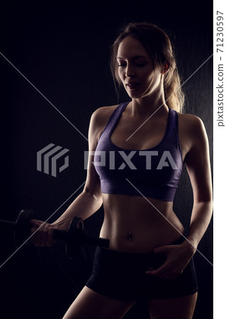 Slim athletic woman Holding dumbbell in the hand on black Slim athletic woman Holding dumbbell in the hand on black 71230597
