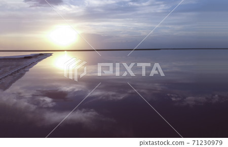 Beautiful sunrise over a pink lake near a small island, the reflection of the blue sky on the water, the purple color of the seascape. 71230979