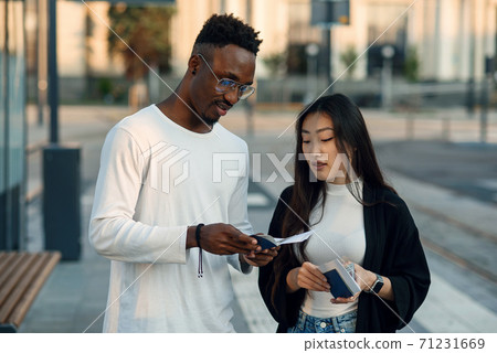 Happy multiracial couple look at boarding pass checking departure time at the stop near airport. Vacations trip concept. 71231669