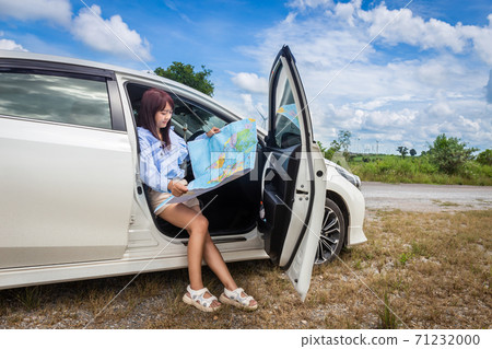 woman in a car looking at a map to reach the holiday destination with blue sky background woman in a car looking at a map to reach the holiday destination with blue sky background 71232000