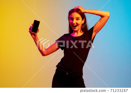 Young caucasian woman's portrait on gradient blue-yellow studio background in neon light 71233287