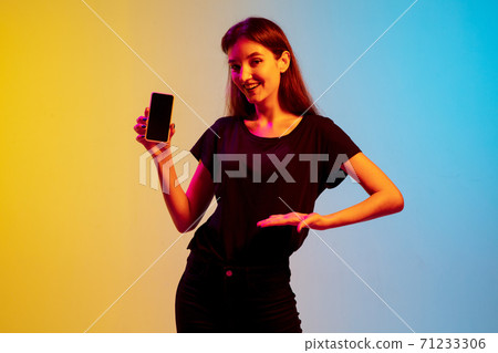 Young caucasian woman's portrait on gradient blue-yellow studio background in neon light Young caucasian woman's portrait on gradient blue-yellow studio background in neon light 71233306