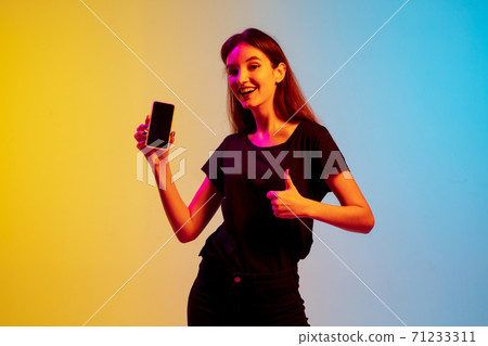 Young caucasian woman's portrait on gradient blue-yellow studio background in neon light 71233311