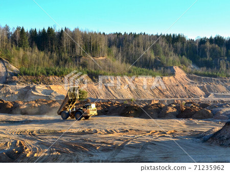 Heavy Yellow Dump Truck Unloads Soil in an Open-cast Mining Sand Pit 71235962