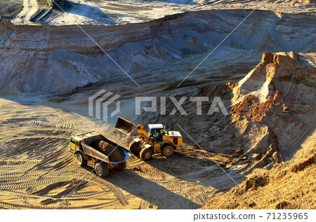 Wheel front-end loader unloading sand into heavy dump truck at the opencast mining quarry Wheel front-end loader unloading sand into heavy dump truck at the opencast mining quarry 71235965