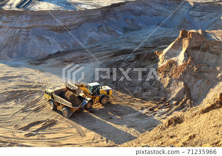 Wheel front-end loader unloading sand into heavy dump truck at the opencast mining quarry Wheel front-end loader unloading sand into heavy dump truck at the opencast mining quarry 71235966