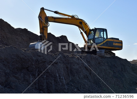 Excavator working at open pit mining. Backhoe digs gravel in sand quarry on blue sky background.  71236596