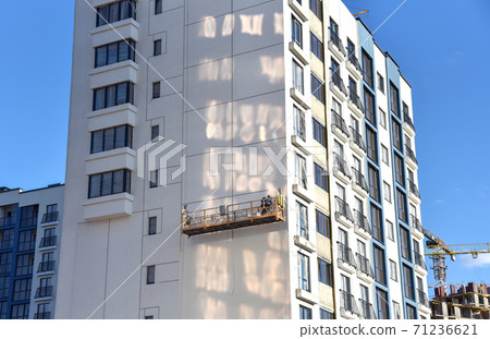 Builder on suspended construction cradle paint the shasad of a new residential building. Builder on suspended construction cradle paint the shasad of a new residential building. 71236621