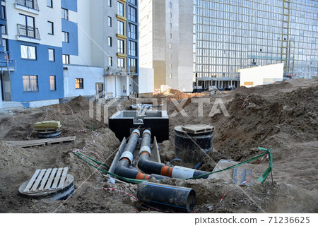 Laying heating pipes in a trench at construction site. Install underground storm systems  71236625