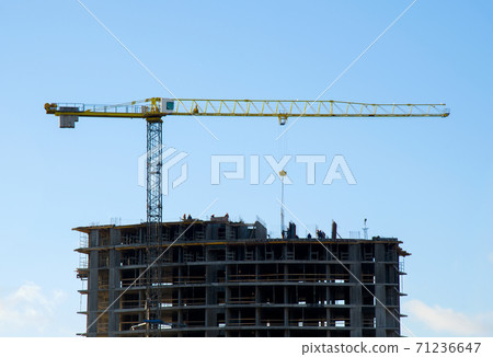 Tower cranes constructing a new residential building at a construction site against blue sky. Tower cranes constructing a new residential building at a construction site against blue sky. 71236647