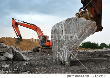 A heavy excavator in a working at granite quarry unloads old concrete stones for crushing  71239418