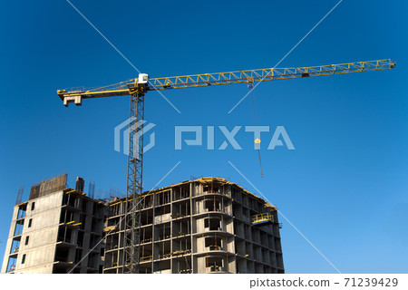 Tower cranes constructing a new residential building at a construction site against blue sky.  71239429