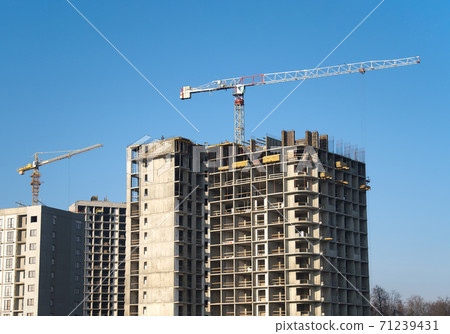 Tower crane constructing a new residential building at a construction site against blue sky. Tower crane constructing a new residential building at a construction site against blue sky. 71239431