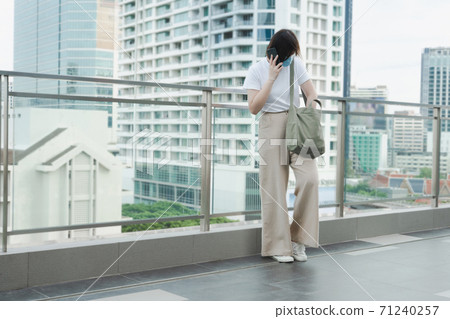 solo asian woman wear protective mask during use phone and relax at rooftop with city background solo asian woman wear protective mask during use phone and relax at rooftop with city background 71240257