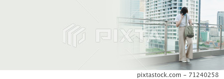solo asian woman wear protective mask during use phone and relax at rooftop with city background 71240258