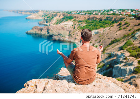 Tourist man outdoor on edge of cliff seashore Tourist man outdoor on edge of cliff seashore 71241745