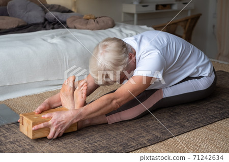 Senior caucasian woman practicing yoga, sitting in Seated forward bend exercise, paschimottanasana pose Senior caucasian woman practicing yoga, sitting in Seated forward bend exercise, paschimottanasana pose 71242634