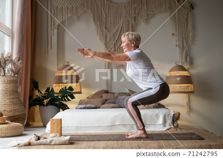 Senior woman practicing advanced yoga Chair Pose Utkatasana Senior woman practicing advanced yoga Chair Pose Utkatasana 71242795