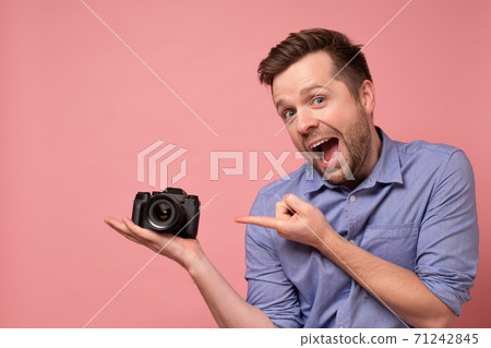 handsome young man holding photocamera on one hand, pointing on it with index finger. handsome young man holding photocamera on one hand, pointing on it with index finger. 71242845
