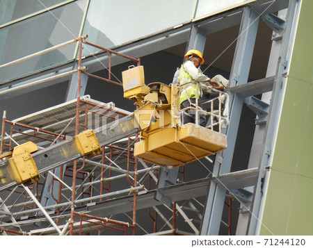 SELANGOR, MALAYSIA -FEBRUARY 16, 2017: Construction workers using mobile crane bucket while working at high level in the construction site. The bucket movement control by the workers himself. SELANGOR, MALAYSIA -FEBRUARY 16, 2017: Construction workers using mobile crane bucket while working at high level in the construction site. The bucket movement control by the workers himself. 71244120