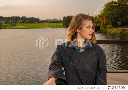 young stand near the water smiling at the camera with a charming smile in a coat in the fall on the dock in the afternoon young stand near the water smiling at the camera with a charming smile in a coat in the fall on the dock in the afternoon 71244509