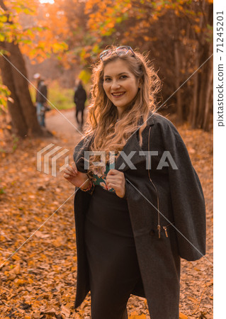 A Cheerful girl in a black cloak stands in chameleon glasses in autumn. Yellow forest, green grass, blonde. with charismatic appearance urban life concept 71245201