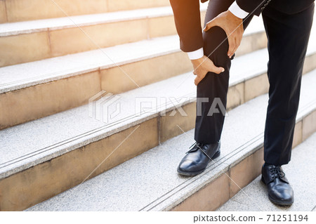The businessman is walking up the stairs, he has a lot of knee pain. The businessman is walking up the stairs, he has a lot of knee pain. 71251194