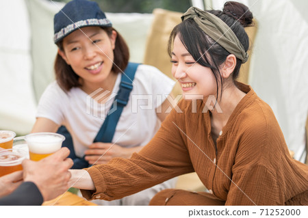 Asian woman toasting with beer after barbecue at campsite 71252000