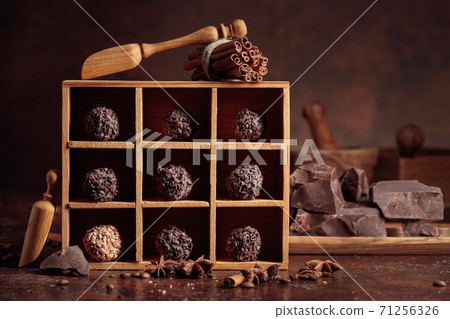 Chocolate candy in wooden box, broken pieces of chocolate, cinnamon sticks, anise and coffee beans. 71256326