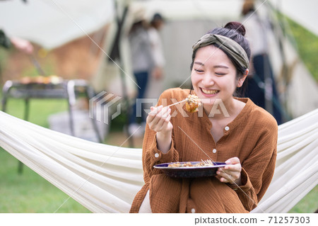 Asian woman eating takoyaki while riding a hammock at a campsite Asian woman eating takoyaki while riding a hammock at a campsite 71257303