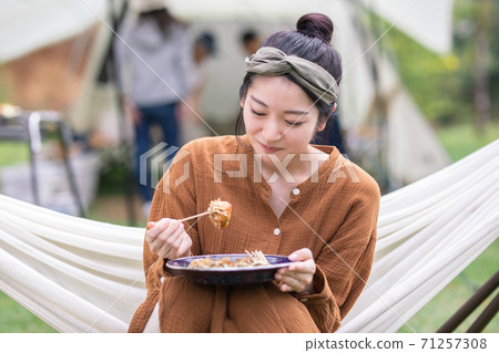 Asian woman eating takoyaki while riding a hammock at a campsite Asian woman eating takoyaki while riding a hammock at a campsite 71257308