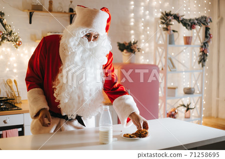 Santa Claus eating cookie and drinking milk at Christmas Santa Claus eating cookie and drinking milk at Christmas 71258695