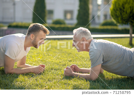 Young male and grey-haired male standing in plank, looking at each other 71258795