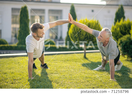 Brown-haired male and grey-haired male standing in plank pose, giving high five 71258796