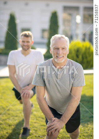 Young male and mature grey-haired male stretching legs outside, hands on knee, smiling 71258837