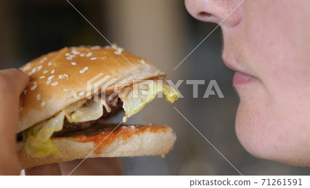 Young Hungry Woman Biting Vegan Meatless Burger in Fast Food Restaurant. Girl eating a hamburger. close-up shot. Fast food eats. Burger in female hands. Young Hungry Woman Biting Vegan Meatless Burger in Fast Food Restaurant. Girl eating a hamburger. close-up shot. Fast food eats. Burger in female hands. 71261591