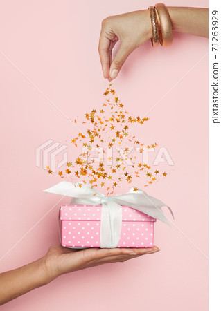 Xmas gift and Christmas tree made from falling golden confetty stars on pastel pink background Xmas gift and Christmas tree made from falling golden confetty stars on pastel pink background 71263929