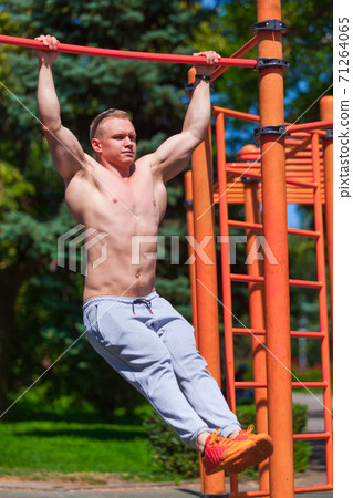 Strong muscular man with a bare torso pulls himself up on a crossbar. Working out outdoors in summer park Strong muscular man with a bare torso pulls himself up on a crossbar. Working out outdoors in summer park 71264065