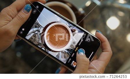 Close up of woman holds modern smartphone and taking pictures of cocoa to share photos on social media resources 71264253