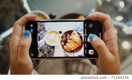Close up of woman holds modern smartphone and taking pictures of her morning breakfast coffee and tasty croissant buns to share photos on social media resources Close up of woman holds modern smartphone and taking pictures of her morning breakfast coffee and tasty croissant buns to share photos on social media resources 71264256