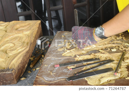 PUTRAJAYA, MALAYSIA - DECEMBER 07,2017: A man is carving wood using traditional hand tools. Carvings based on flora motifs 71264787