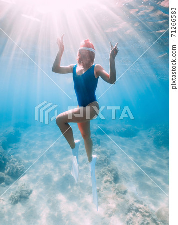 Christmas holidays party with freediver. Happy freediver woman with New year cap glides underwater with fins in blue ocean. Christmas holidays party with freediver. Happy freediver woman with New year cap glides underwater with fins in blue ocean. 71266583