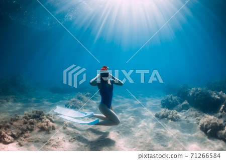 Christmas holidays party with freediver. Happy freediver woman with New year cap glides underwater with fins in blue ocean. Christmas holidays party with freediver. Happy freediver woman with New year cap glides underwater with fins in blue ocean. 71266584