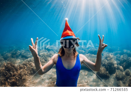 Freediver woman with Christmas cap posing underwater in blue sea. Christmas holidays Freediver woman with Christmas cap posing underwater in blue sea. Christmas holidays 71266585