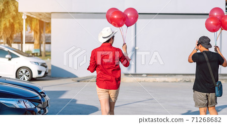 Back view of gay man in red shirt holding red balloons from the car park to join the party in the afternoon. 71268682
