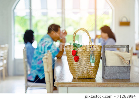 Mini portable alcohol gel bottle to kill Corona Virus(Covid-19) and artificial strawberries hanging on a bamboo purse on table with blurred image of a family eating at home in background. 71268984