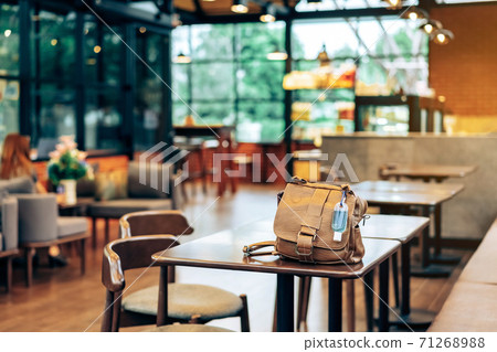 Mini portable alcohol gel bottle to kill Corona Virus(Covid-19) hang on a brown leather shoulder bag on table in coffee shop.New normal lifestyle. Health care concept. Selective focus on alcohol gel 71268988