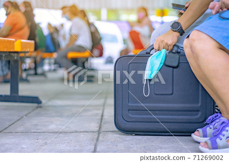 Male tourist prepare to carry luggage and surgical mask to prevent Corona Virus(Covid-19) to travel by public transport at transport station. New normal lifestyle, Selective focus on surgical mask. Male tourist prepare to carry luggage and surgical mask to prevent Corona Virus(Covid-19) to travel by public transport at transport station. New normal lifestyle, Selective focus on surgical mask. 71269002