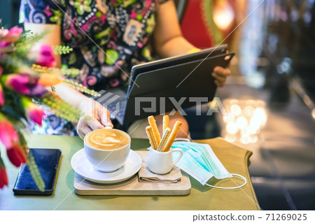 Hot Cappuccino coffee with protective mask on a wooden table for people being quarantined in the situation of the spread of the corona virus (Covid-19).  New normal lifestyle concept. Selective focus 71269025