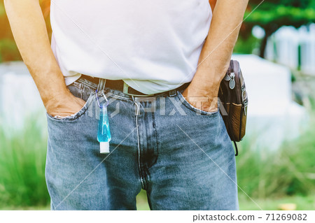 Mini portable alcohol gel bottle to kill Corona Virus(Covid-19) hanging on belt loop of man' s jeans with plants background. New normal lifestyle. Health care concept. Selective focus on alcohol gel 71269082